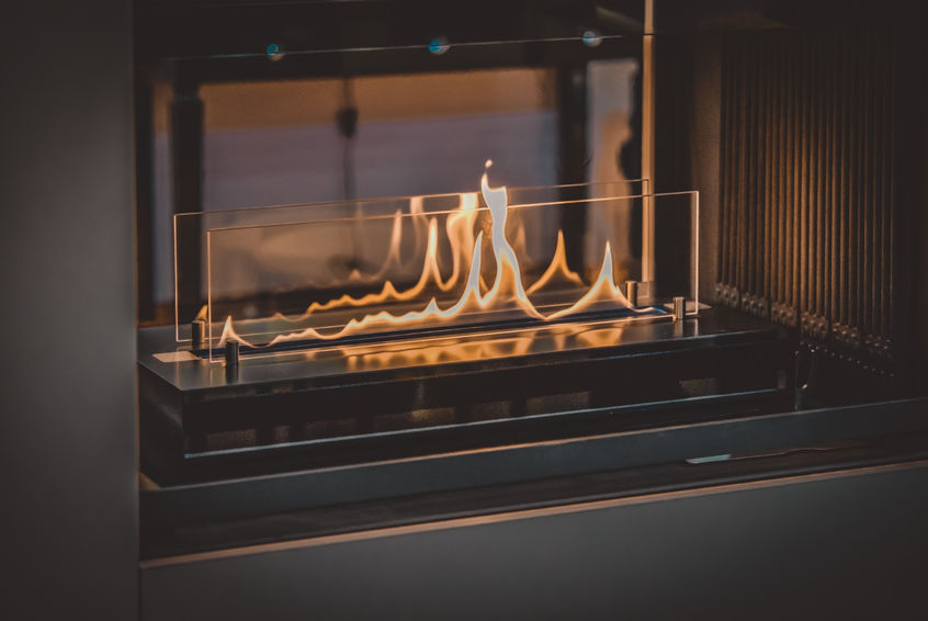 Modern indoor fireplace with visible flames behind a transparent protective glass barrier.